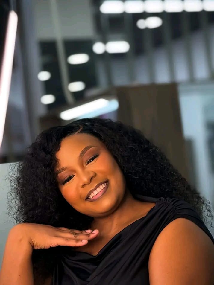 Client smiling with a curly wig install and soft glam makeup